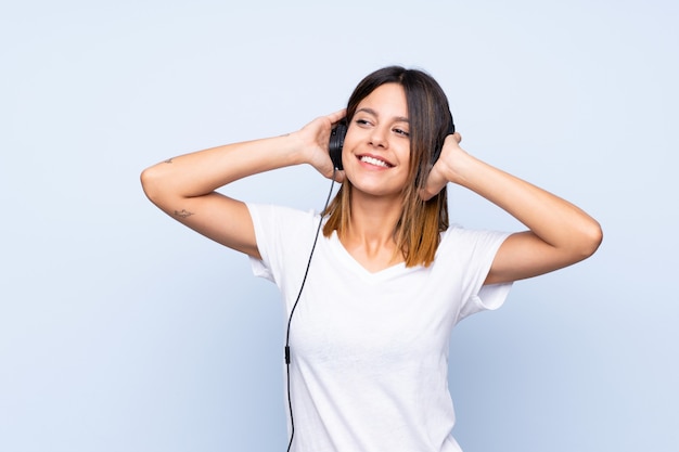 Young woman over isolated blue wall using the mobile with headphones