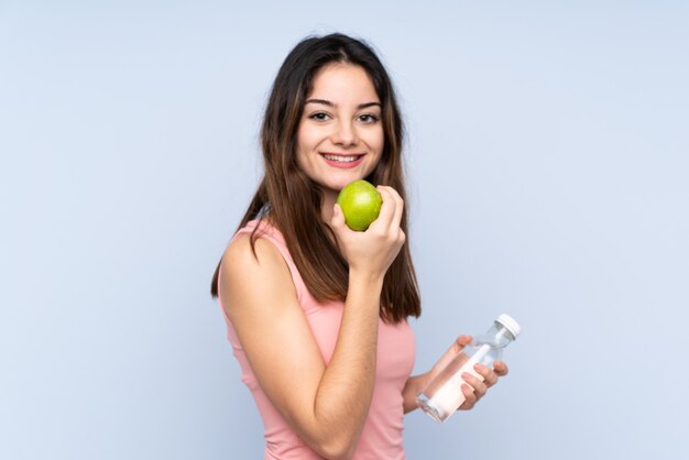 Молодая женщина изолированная на сини с яблоком и с бутылкой воды