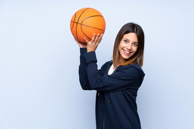 Young woman over isolated blue with ball of basketball