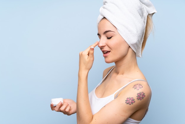 Young woman over isolated blue  with moisturizer