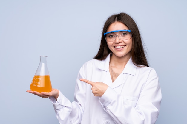 Young woman over isolated blue with a scientific test tube and pointing it