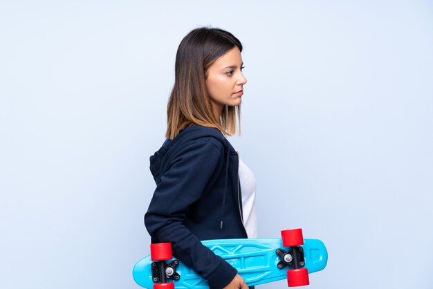 Young woman over isolated blue with skate in back position