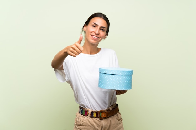 Young woman over isolated green wall holding gift box