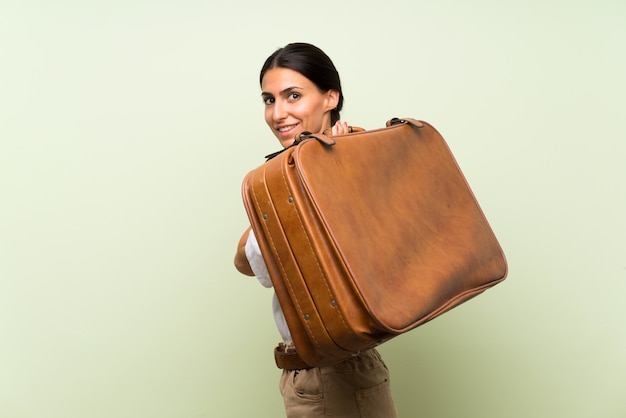 Young woman over isolated green wall holding a vintage briefcase