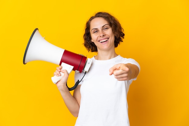 Young woman isolated holding a megaphone and smiling while pointing to the front