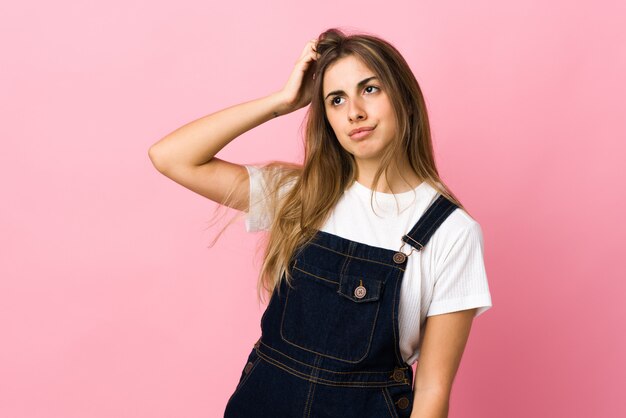 Young woman over isolated pink background having doubts while scratching head