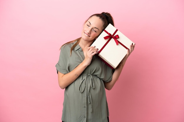 Young woman isolated on pink background pregnant and holding a gift