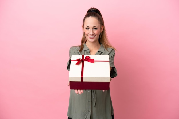 Young woman isolated on pink background pregnant and holding a gift