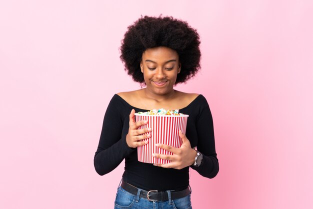 Young woman isolated on pink holding a big bucket of popcorns