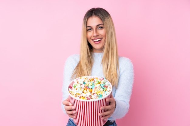 Young woman over isolated pink wall holding a big bucket of popcorns