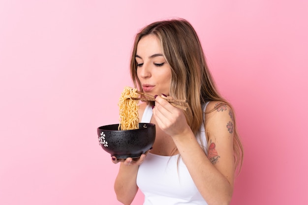 Foto giovane donna sopra la parete rosa isolata che tiene una ciotola di tagliatelle con la sabbia della bacchette che la soffia perché sono calde