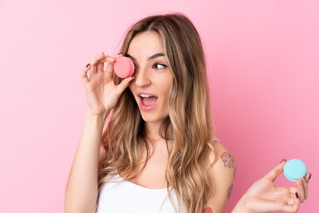 Foto giovane donna sopra la parete rosa isolata che tiene i macarons francesi variopinti