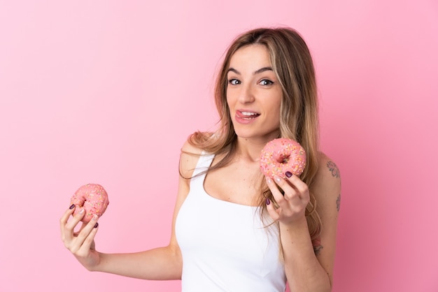 도넛을 들고 고립 된 분홍색 벽에 젊은 여자
