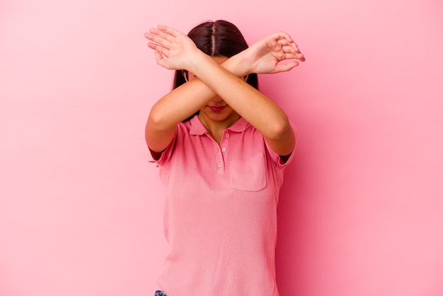 Молодая женщина изолирована на розовой стене, скрестив две руки