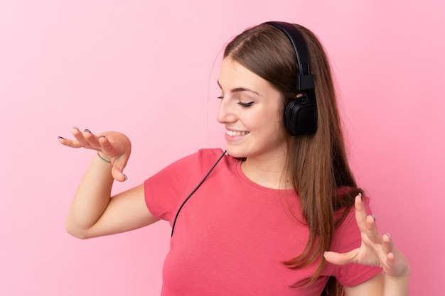Молодая женщина над изолированной розовой стеной слушая музыку и танцы