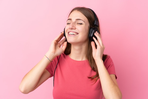 Young woman over isolated pink wall listening music and singing