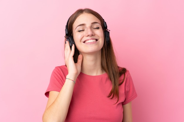 Giovane donna sopra musica d'ascolto isolata della parete rosa