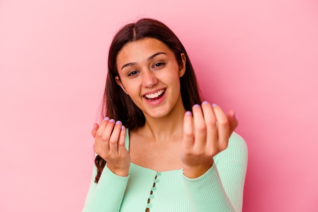 Giovane donna isolata sul muro rosa che punta il dito contro di te come se invitando ad avvicinarsi