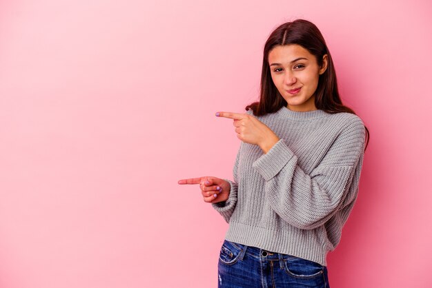 Young woman isolated on pink wall pointing with forefingers to a copy space, expressing excitement and desire