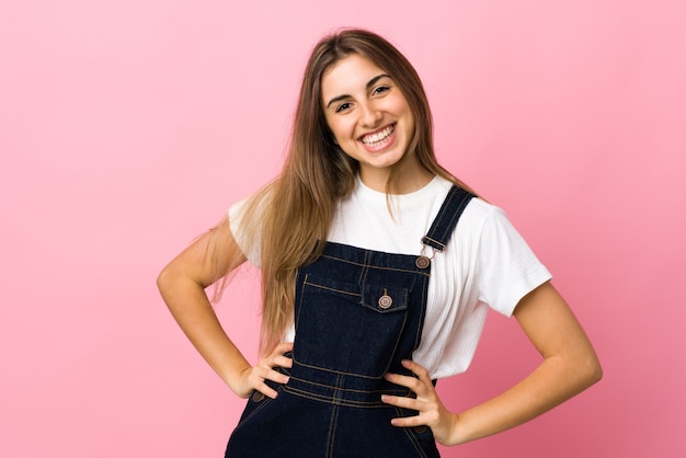 Young woman over isolated pink wall posing with arms at hip and smiling