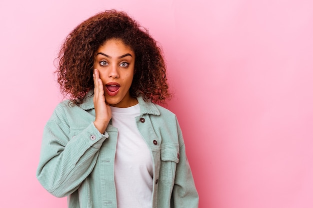 Young woman isolated on pink wall shouts loud, keeps eyes opened and hands tense