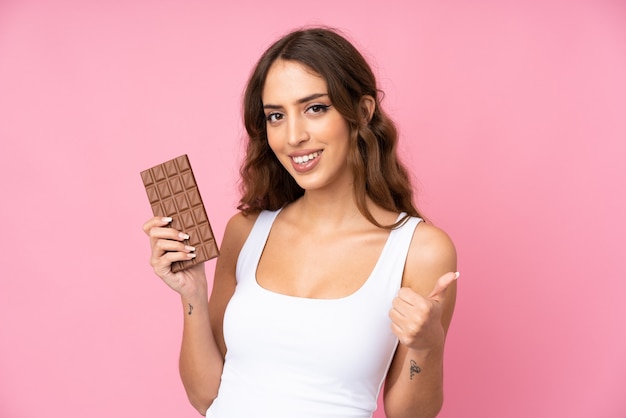 Photo young woman over isolated pink wall taking a chocolate tablet and with thumb up