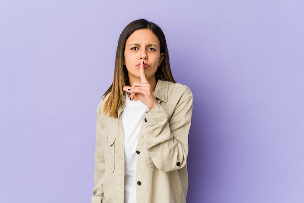 Young woman isolated on purple background keeping a secret or asking for silence.