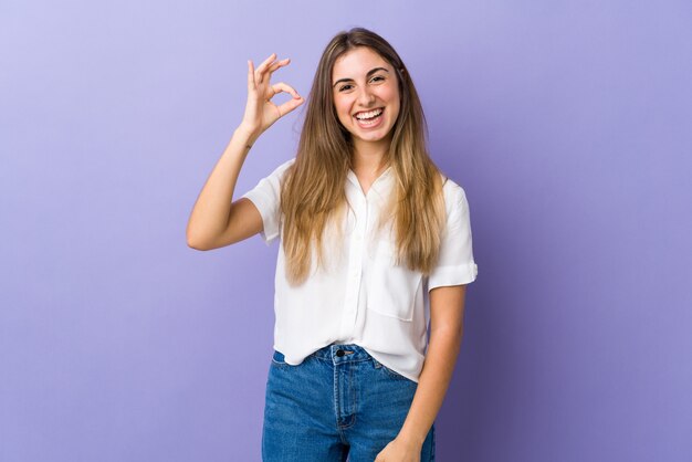 Young woman over isolated purple background showing ok sign with fingers