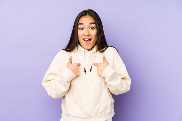 Young woman isolated on a purple background surprised pointing with finger, smiling broadly.