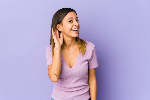 Young woman isolated on purple background trying to listening a gossip.