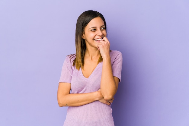 Young woman isolated on purple space relaxed thinking about something looking at a copy space.