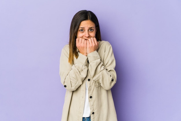 Young woman isolated on purple wall biting fingernails, nervous and very anxious.