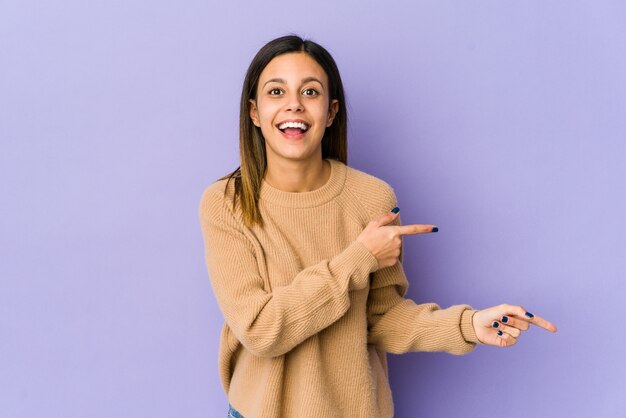 Young woman isolated on purple wall excited pointing with forefingers away