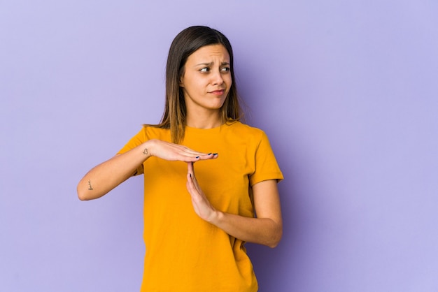 Young woman isolated on purple wall showing a timeout gesture.