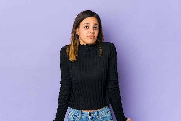 Young woman isolated on purple wall shrugs shoulders and open eyes confused