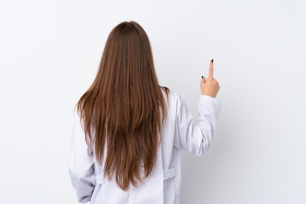 Молодая женщина над изолированной стеной носить платье доктора и указывая назад