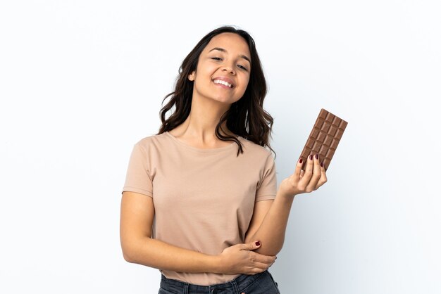 Young woman over isolated white background taking a chocolate tablet and happy