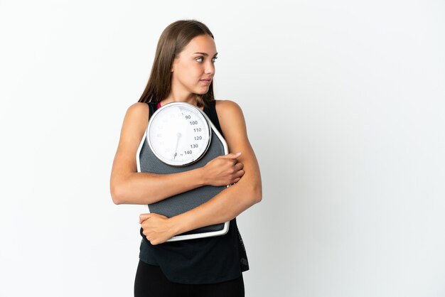 Young woman over isolated white background with weighing machine and looking side