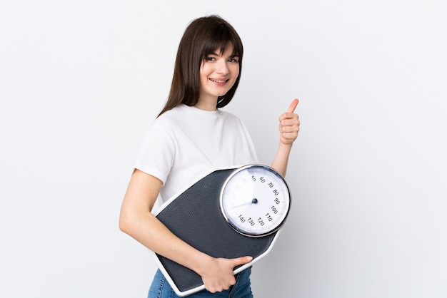 Young woman isolated on white holding weighing machine with thumb up