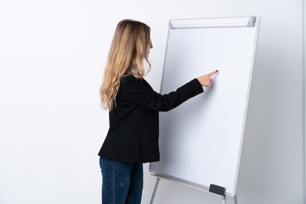 Young woman over isolated white wall giving a presentation on white board and writing in it