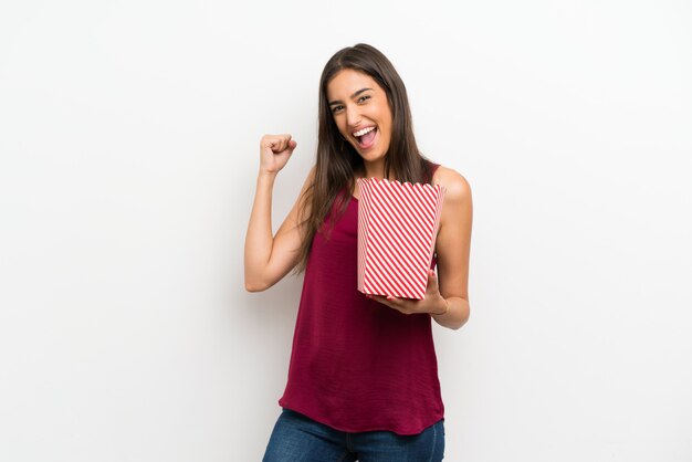 Young woman over isolated white wall holding a bowl of popcorns