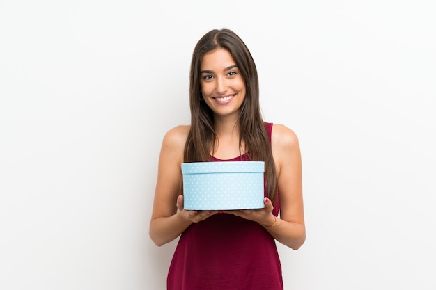 Young woman over isolated white wall holding gift box