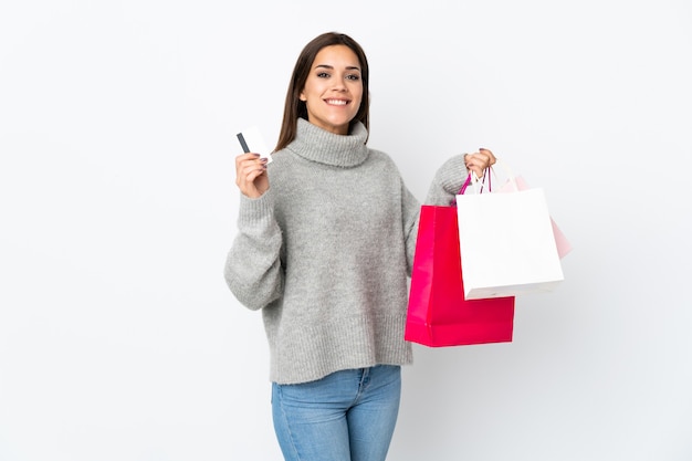 Young woman isolated on white wall holding shopping bags and a credit card