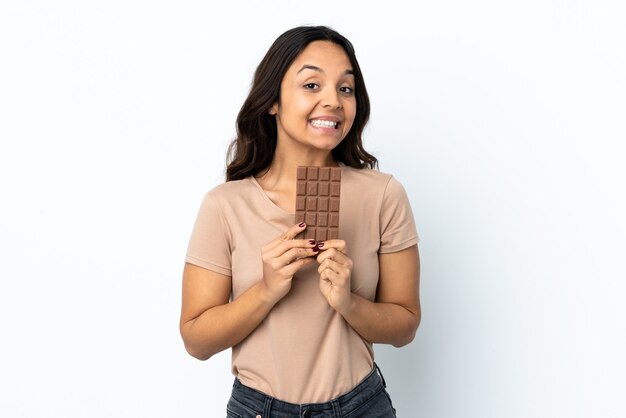 Young woman over isolated white wall taking a chocolate tablet and happy