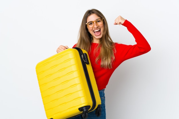 Young woman over isolated white wall in vacation with travel suitcase