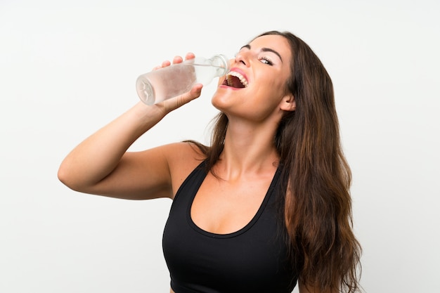 Молодая женщина над изолированной белой стеной с бутылкой воды