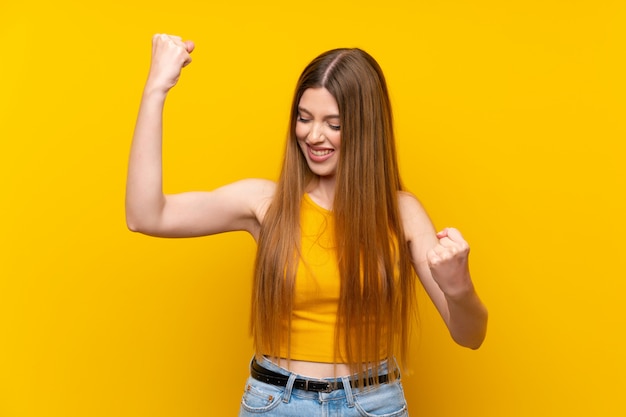 Giovane donna sopra isolato sfondo giallo che celebra una vittoria