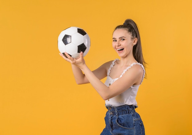 Young woman over isolated yellow background holding a soccer ball