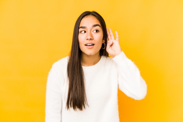 Young woman isolated on a yellow background trying to listening a gossip