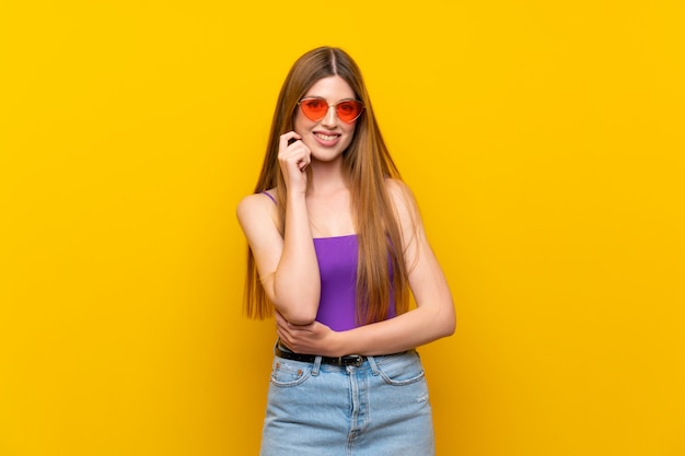 Young woman over isolated yellow background with glasses and smiling